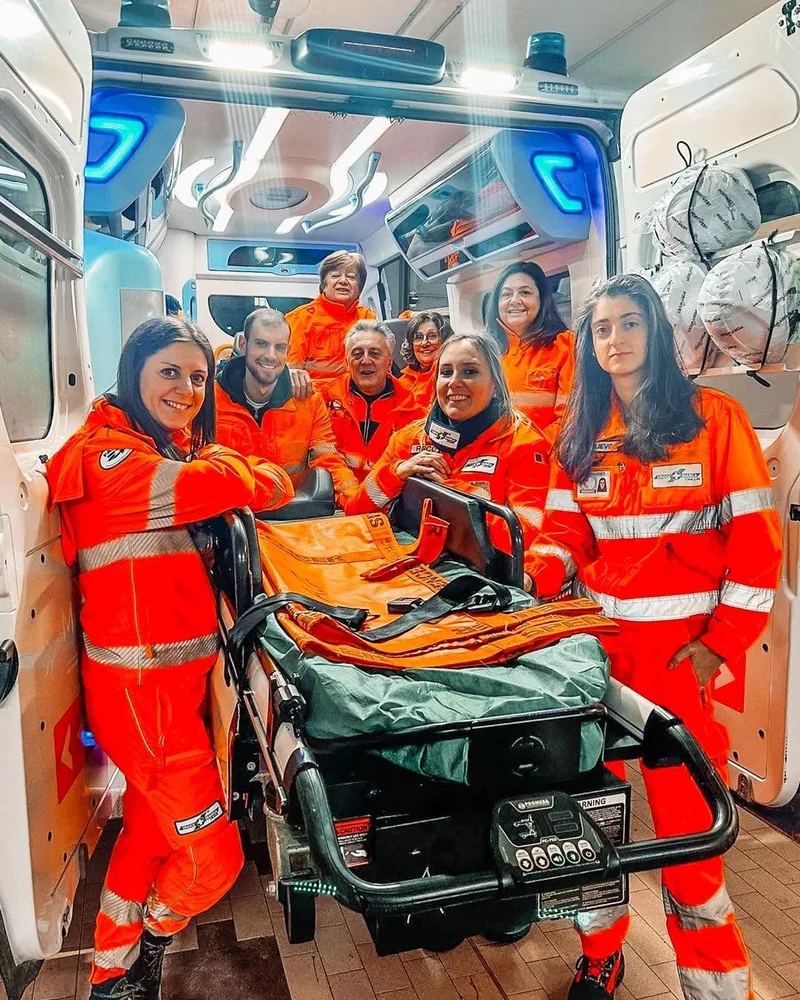 Volontari in divisa sull'ambulanza, attorno alla barella